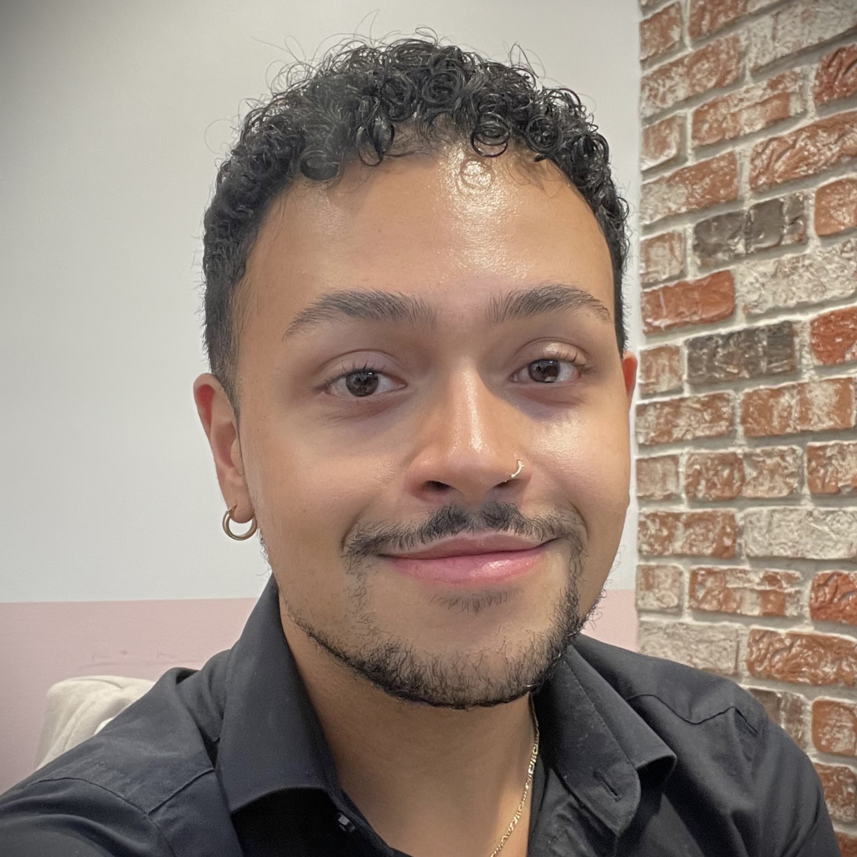 Smiling man with nose ring near brick wall